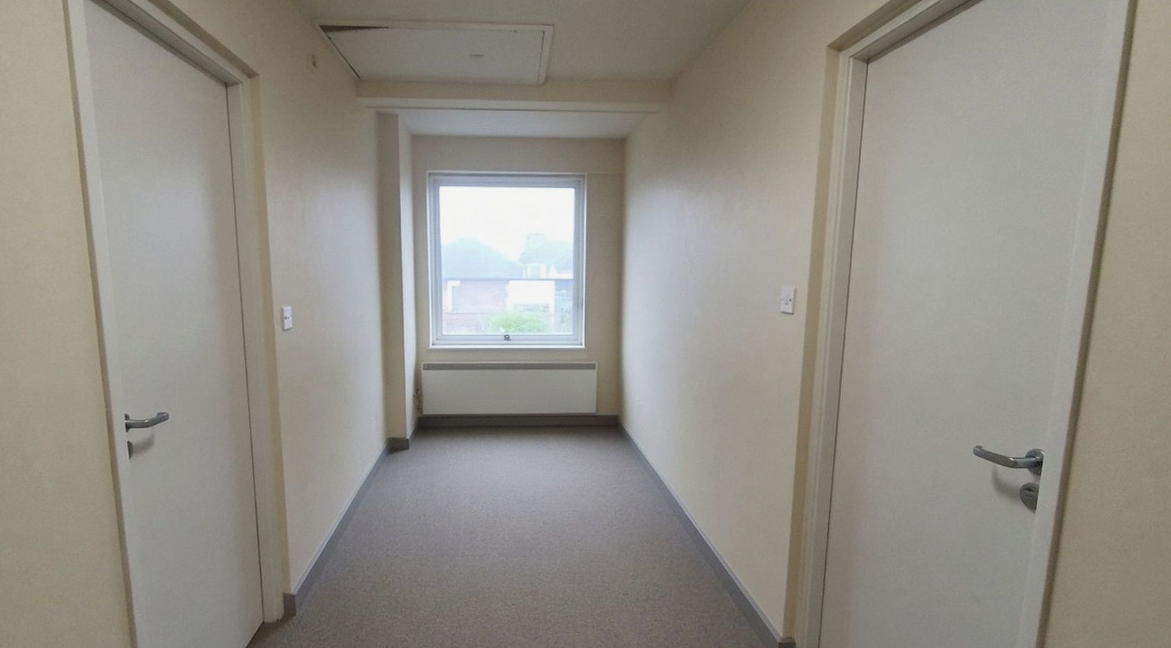 Short hotel corridor with blank doors and a window at the far end